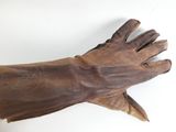 Quelqu'un tient une paire de gants en cuir marron posés sur une surface blanche.