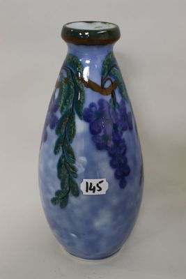 a blue vase with purple grapes on it on a white surface