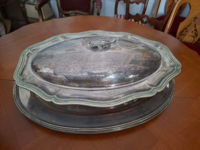 un plateau en argent muni d'un couvercle en verre, posé sur une table en bois