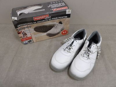 Il y a deux paires de chaussures blanches sur un lit, à côté d'une boîte à chaussures.