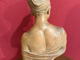 statue of a woman sitting on a wooden table with a pink background
