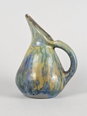 un vase bleu et vert muni d'une anse, posé sur une surface blanche