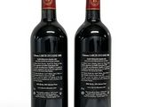 two bottles of red wine sitting next to each other on a white surface