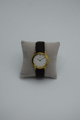 un gros plan d'une montre-bracelet posée sur un oreiller, sur une surface blanche