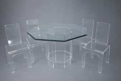 une table en verre entourée de quatre chaises, sur fond gris
