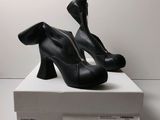 des chaussures à talons hauts noires posées sur une boîte blanche, elle-même posée sur une surface blanche