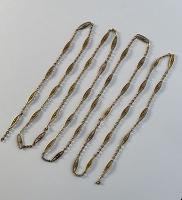 un ensemble de cinq colliers à chaîne en or posés sur une surface blanche
