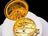 a gold pocket watch on a white plate on a black background