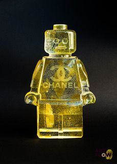 petit bonhomme Lego jaune arborant le logo Chanel, debout devant un fond noir