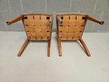 two wooden chairs with leather straps on them sitting on a white surface