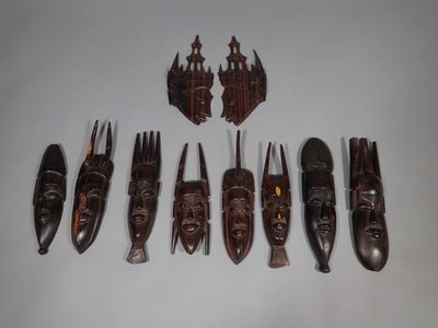 Plusieurs masques en bois sont disposés en rangée sur une surface blanche
