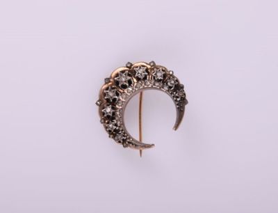 Gros plan sur une broche en forme de croissant en or, sertie de diamants noirs et blancs