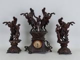 trois figurines de chevaux en bronze et une horloge posées sur une table