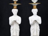 pair of white statues holding cups and saucers on top of each other