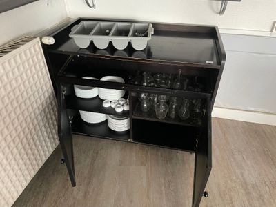 un petit meuble noir sur lequel sont posés de la vaisselle et des tasses