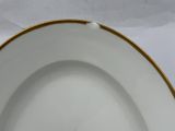 an empty white plate with a gold rim on a white table