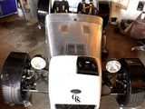 une petite voiture blanche dans un garage, avec d'autres voitures en arrière-plan