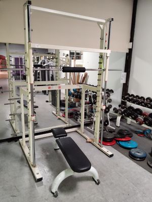 une photo d'une salle de sport avec un banc, des haltères et d'autres appareils