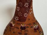 a brown vase with flowers on it on a white surface