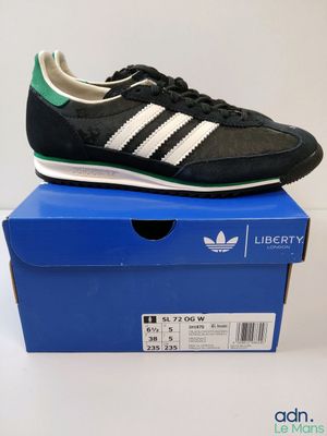 une paire de baskets noires et vertes posée sur une boîte bleue