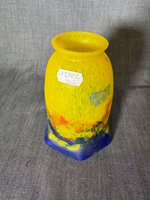 un vase jaune au pied bleu posé sur une surface grise