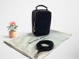 Le petit sac noir se trouve à côté d'une petite fleur rose et d'un sac blanc.