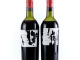 two bottles of red wine sitting next to each other on a white surface