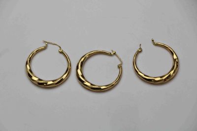 trois paires de boucles d'oreilles créoles en or sur fond blanc
