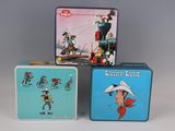 three tin lunch boxes with cartoon characters on them sitting on a table