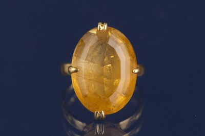 une image représentant une bague ornée d'une pierre jaune sur un fond noir