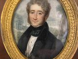 portrait of a man in a black coat and bow tie in a gold frame on a table