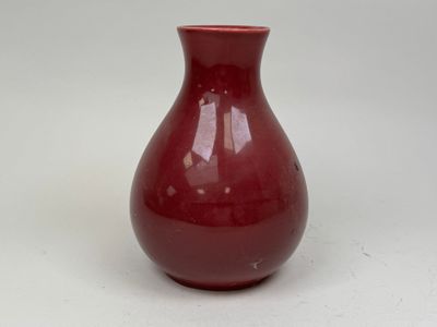 un vase rouge posé sur une surface blanche