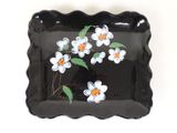 a black plate with white and orange flowers painted on it