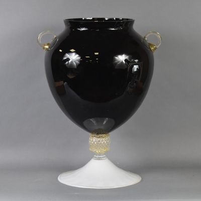 a black vase with gold handles on a white pedestal