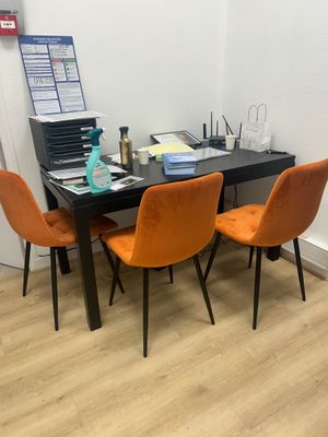 une table noire avec des chaises orange et un ordinateur portable posé dessus