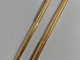 two gold colored pens sitting on top of each other on a table