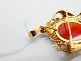 une photo d'une broche rouge et dorée posée sur un fond blanc