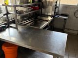 une table en acier inoxydable sur laquelle sont posés des casseroles et des poêles, dans une cuisine