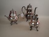 two silver teapots and a coffee pot sitting on a table