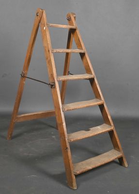 Un vieil escabeau en bois est appuyé contre un mur gris.