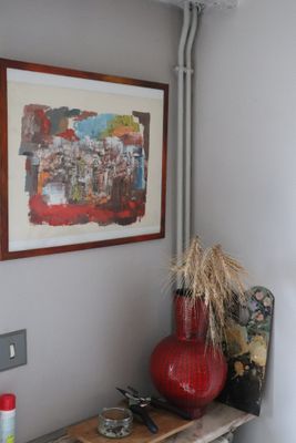 a red vase sitting on a wooden shelf next to a painting