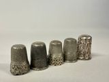 six antique thimbles lined up in a row on a white surface