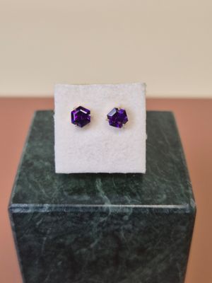 une paire de boucles d'oreilles « cubicge » violettes posées sur un bloc de marbre