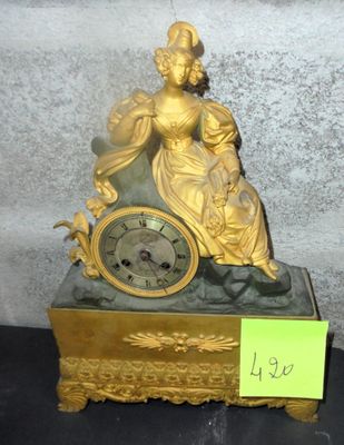a gold clock with a woman sitting on top of it