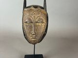 un masque doré muni de cornes, posé sur un socle noir