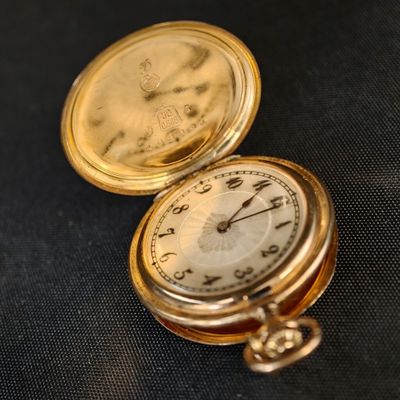 une montre de poche en or posée sur un tissu noir