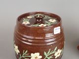 a brown jar with white flowers on it next to a small bowl