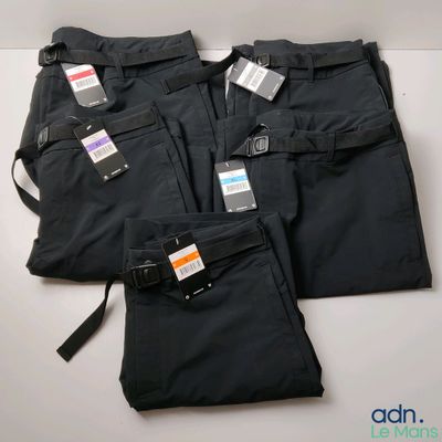 trois paires de pantalons noirs, encore étiquetés, posées sur une table