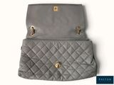 the back of a grey purse with gold hardware on it