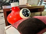 a clock sitting on top of a table next to a pillow